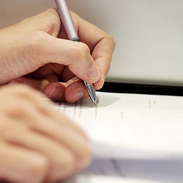 person writing with pen on a printed piece of paper